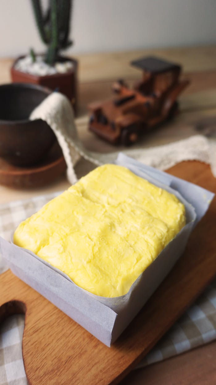 A slab of fresh yellow butter on a wooden cutting board with rustic decor in the background.