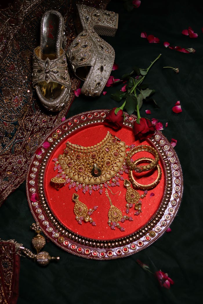 Flat lay of exquisite traditional jewelry set on a red velvet tray, adorned with flowers and footwear.
